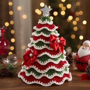 May include: A crocheted Christmas tree decoration featuring alternating tiers of red and green yarn with white scalloped edges. The tree is adorned with small white pearl-like beads and two large red satin bows, topped with a silver glittery star.