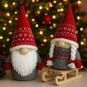 Pode incluir: Dois gnomos de Natal de malha com chapéus vermelhos e brancos estampados, corpos cinzentos e longas barbas brancas. Um gnomo tem uma longa barba branca e o outro tem tranças brancas. Eles são colocados em um fundo de luzes de Natal e um trenó de madeira.