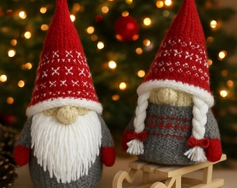 May include: Two plush gnome figurines with red knit hats featuring white patterns. One gnome has a long white beard, while the other has two white braided pigtails and sits on a small wooden sled. Both wear grey sweaters and red mittens.