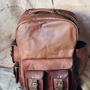 Peut inclure: Un sac à dos en cuir marron avec plusieurs poches et compartiments. Le sac à dos a deux poches avant avec boucles, des poches latérales et une poignée supérieure. Le cuir a un aspect texturé et une esthétique vintage.