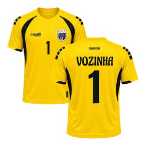 Puede incluir: Una camiseta de fútbol de color amarillo brillante con paneles laterales negros y mangas cortas. El frente presenta el logotipo de Capelli Sport, el escudo de la FCF y el número 1. La espalda muestra el texto CABO VERDE y el nombre VOZINHA sobre el 1.