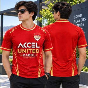 May include: A red short-sleeved athletic shirt featuring yellow accents and the text "AKCEL UNITED KABUL" in white and gold lettering. The shirt includes a shield-shaped logo on the chest and a matching design on the back, paired with black shorts.