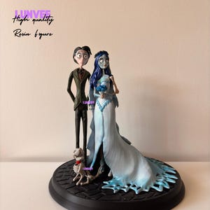 Könnte beinhalten: Ein Harzfiguren-Set mit einer Braut und einem Bräutigam mit einem Skeletthund. Die Braut trägt ein blaues Hochzeitskleid mit langer Schleppe, und der Bräutigam ist in einem schwarzen Anzug. Der Sockel ist schwarz und rund. Der Text auf dem Bild lautet "High quality Resin figure."