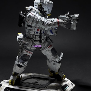 May include: A white and grey sci-fi action figure in a tactical suit with a helmet, holding a futuristic pistol. The figure features red and blue accents, a backpack, and stands on a detailed hexagonal base with the text LUNVEE printed on the leg.