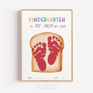 May include: A rectangular print in a wooden frame featuring a slice of bread illustration with two red footprints in the center. The text reads "KINDERGARTEN IS TOE-TALLY MY JAM!" with "Name :" and "Date: / /" at the bottom on a grid background.