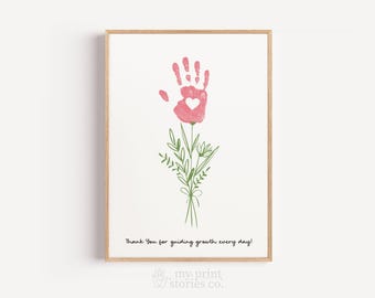May include: Framed print featuring a pink handprint with a heart, resembling a flower. Green leaves and stems are tied with a bow. The text reads, "Thank You for guiding growth every day!"