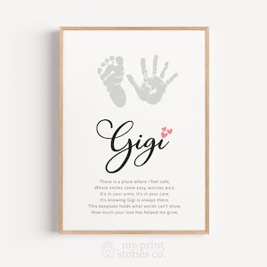 May include: Framed print with a light wood frame. The print features a baby footprint and handprint in gray, with the name "Gigi" in cursive. Small pink hearts accent the name. A poem is printed below the name.