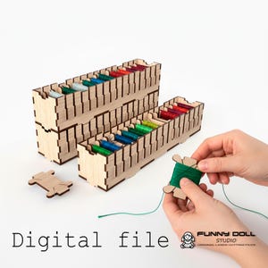 Op de afbeelding: Houten draadorganizers gevuld met kleurrijke spoelen draad. De afbeelding toont twee gestapelde organizers, een losse spoel en een hand die een spoel groen draad vasthoudt. De tekst "Digital file" staat onderaan.