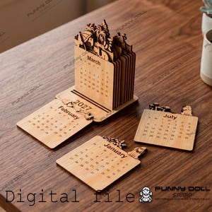 May include: A light-coloured wooden desk calendar for 2027 featuring laser-cut designs. The set includes a vertical block with monthly pages and separate flat wooden panels for January, February, and July, each displaying dates and small animal silhouettes.