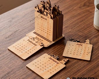 May include: A light-colored wooden desk calendar for 2027 featuring laser-cut designs. The set includes a vertical block with monthly pages and separate flat wooden panels for January, February, and July, each displaying dates and small animal silhouettes.