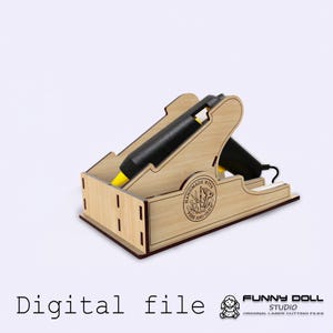 Puede incluir: Un soporte de madera de color marrón claro para pistola de pegamento, con dos pistolas de pegamento negras con puntas amarillas. El soporte tiene el texto "HANDMADE WITH FIRE AND GLUE". Las palabras "Digital file" están en la parte inferior.