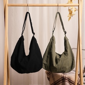 Peut inclure: Deux sacs à bandoulière de style hobo en toile, l'un noir uni et l'autre vert olive. Chaque sac présente une large bandoulière intégrée avec un mécanisme de boucle réglable, un compartiment principal profond et une base incurvée.