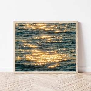 Pode incluir: Uma caneca de cerâmica branca com uma alça preta e o texto "But First, Coffee" em negrito preto. A caneca está sobre uma superfície branca, mostrando seu design limpo.