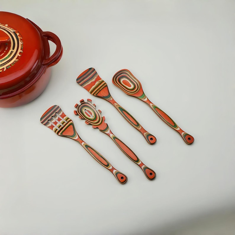 May include: Four wooden kitchen utensils with orange, green, and brown layered designs. The set includes a spatula, slotted spoon, and two other spoon-like tools. A red cooking pot with a lid is in the background.