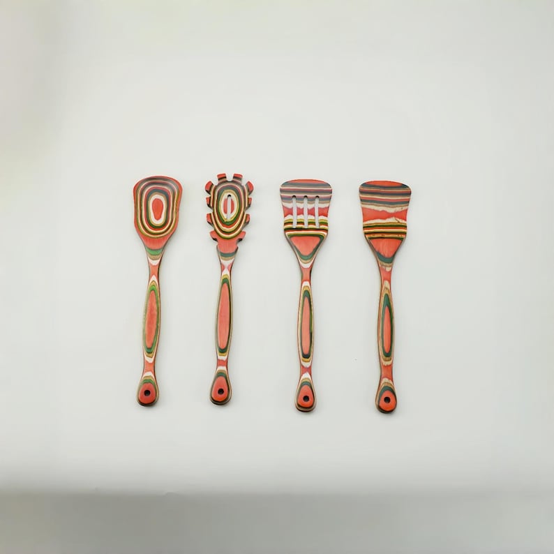 May include: Four wooden kitchen utensils with red, orange, and green accents. The set includes a spoon, a slotted spoon, and two spatulas. Each utensil has a unique design on the head and a long handle.