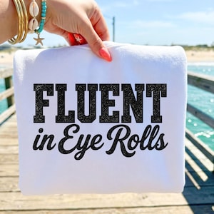 May include: A white sweatshirt featuring the black text "FLUENT in Eye Rolls" printed on the front. The word "FLUENT" is in a bold, block-style font, while "in Eye Rolls" is written in a cursive script font. The fabric is plain white.