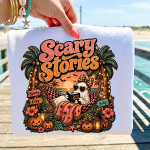 以下が含まれることがあります： 「Scary Stories」と書かれたカラフルなグラフィックが特徴の白いスウェットシャツ。サングラスをかけたお化けがハンモックで本を読んでいるデザインで、ヤシの木、カボチャ、海が背景に描かれています。「Spooky」、「Cozy」、「Salty」の文字も含まれています。