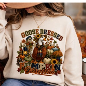 May include: Cream-colored sweatshirt with a fall-themed graphic. The graphic features a goose wearing a hat and scarf, surrounded by pumpkins, sunflowers, and the text "GOOSE DRESSED PUMPKIN OBSESSED".
