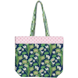 May include: A tote bag featuring a dark blue background with a repeating pattern of green Venus flytraps and white flowers. The top section has a light pink scalloped pattern, and the two shoulder straps feature a green and white checkered design.