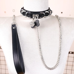 May include: Black leather collar with silver-tone metal accents and a matching leash. The collar features a decorative charm and a chain leash. The leash has a black leather handle.