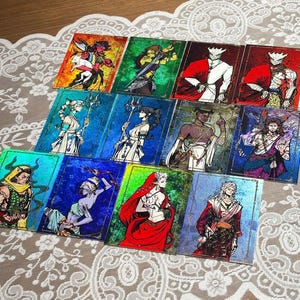 May include: A collection of twelve rectangular trading cards featuring vibrant, foil-accented illustrations of fantasy characters. Each card displays a unique figure in a distinct colour palette, including shades of red, blue, green, and purple.