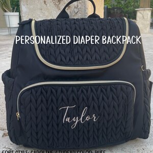 May include: Black quilted diaper backpack with gold zippers and trim. The bag is personalized with the name "Taylor" embroidered in a cursive font. The text "PERSONALIZED DIAPER BACKPACK" is printed on the front.
