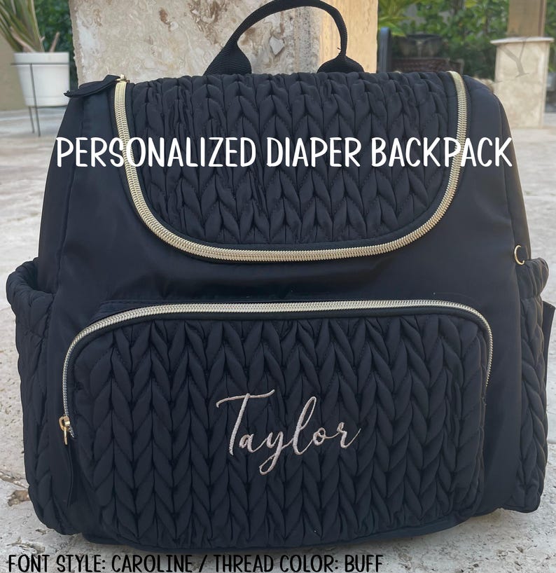 May include: Black quilted diaper backpack with gold zippers and trim. The bag is personalized with the name "Taylor" embroidered in a cursive font. The text "PERSONALIZED DIAPER BACKPACK" is printed on the front.