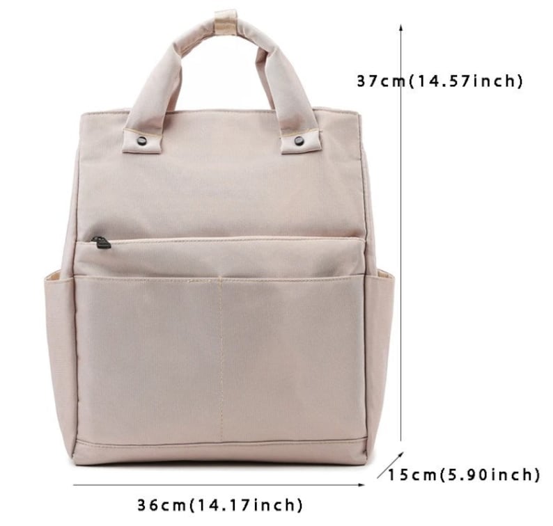 May include: A beige backpack with a top handle and two side pockets. The bag is 14.17 inches wide, 14.57 inches tall, and 5.90 inches deep. It has a front zippered pocket and two snap closures on the handle.