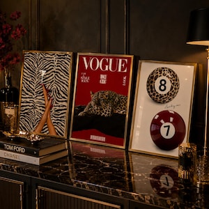 Könnte beinhalten: Drei gerahmte Wandbilder in Goldrahmen. Das linke Bild zeigt Beine in roten High Heels vor einem Zebramuster. Das mittlere Bild ist ein rotes Vogue-Magazin-Cover mit einem Leoparden. Das rechte Bild zeigt eine 8er- und eine 7er-Billardkugel.