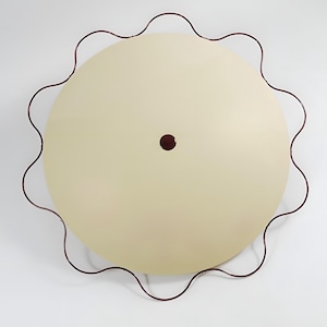 May include: A large, round, cream-colored ceiling light fixture with a wavy, dark red metal frame. The light has a small, dark red dot in the center. The fixture is mounted on a white ceiling.