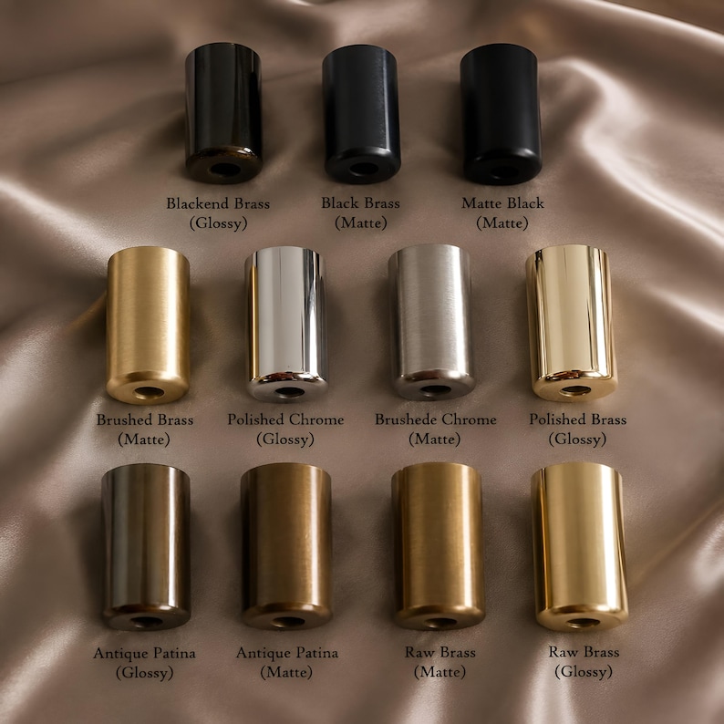 May include: A collection of twelve cylindrical metal hardware knobs arranged in three rows. The finishes include Blackened Brass, Black Brass, Matte Black, Brushed Brass, Polished Chrome, Brushed Chrome, Polished Brass, Antique Patina, and Raw Brass.