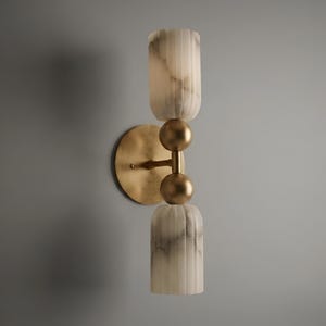 May include: A wall sconce featuring a circular brass backplate and a central vertical rod with two spherical brass accents. The fixture includes two cylindrical, vertically fluted, white and grey marbled glass shades positioned at the top and bottom.
