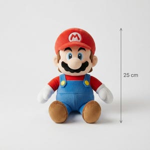 Puede incluir: Un peluche de Mario, de aproximadamente 25 cm de altura, con gorra roja con 'M' blanco, camisa roja, peto azul y zapatos marrones. El mu&ntilde;eco tiene un gran bigote negro y guantes blancos, sobre un fondo neutro.