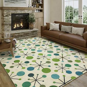 May include: A cream-colored area rug with a mid-century modern design. The rug features a pattern of green and blue circles connected by black lines. The rug is in a living room with a brown leather sofa and a stone fireplace.