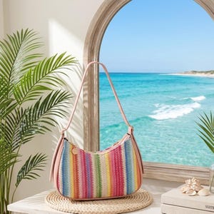 May include: A crescent-shaped shoulder bag featuring a multi-colored vertical striped pattern in shades of pink, yellow, blue, and green. The bag is constructed with a woven texture and includes a solid pink strap and matching pink side panels.