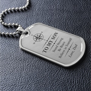 Puede incluir: Un colgante de placa de identificación de metal plateado en una cadena de bolas a juego. La placa presenta una rosa de los vientos grabada y el texto: TO MY SON, Stand Strong, Be Brave, Believe in Yourself, Love, Dad. Acabado metálico cepillado.