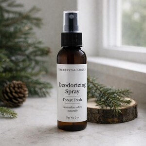 Puede incluir: Una botella de vidrio marrón de spray desodorante "Forest Fresh" con un pulverizador negro. La etiqueta dice "The Crystal Garden" y "Net Wt. 2 oz." La botella está rodeada de ramas de pino y una piña.