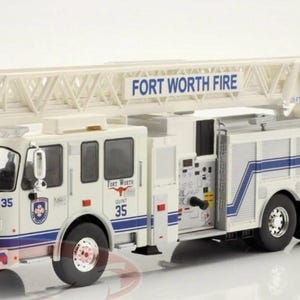 May include: A white and blue model fire truck with a ladder. The words "FORT WORTH FIRE" are printed on the ladder. The number "35" is visible on the side of the truck. The truck has a blue and white striped bumper.