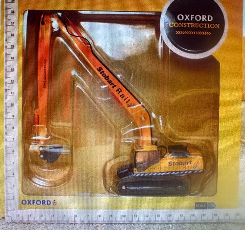 May include: A toy excavator model in a clear plastic package. The excavator is primarily orange and yellow, with black treads and the text "Stobart Rail" and "Oxford Construction". The model is labeled "Civil Engineering".
