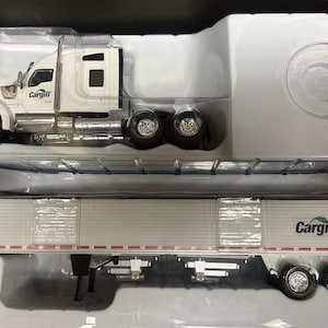 May include: A white semi-truck and trailer model with the "Cargill" logo. The truck has six wheels and a detailed design. The trailer is white with a corrugated texture and the Cargill logo.