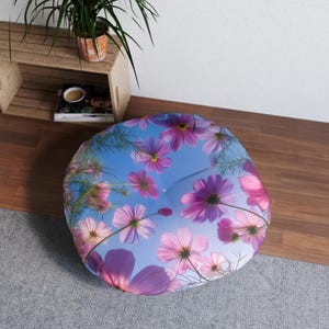 Op de afbeelding: Rond vloerkussen met een bloemenpatroon van roze en paarse kosmosbloemen tegen een lichtblauwe achtergrond. Dit kussen is een decoratief item, perfect om een vleugje natuurlijke decoratie aan elke kamer toe te voegen.