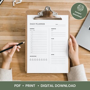 May include: A clipboard with a white daily planner sheet. The planner includes sections for schedule, priorities, to-do list, and notes. A pencil rests on the sheet. The words "Instant download" are in a green circle. The bottom of the image says "PDF • PRINT • DIGITAL DOWNLOAD".