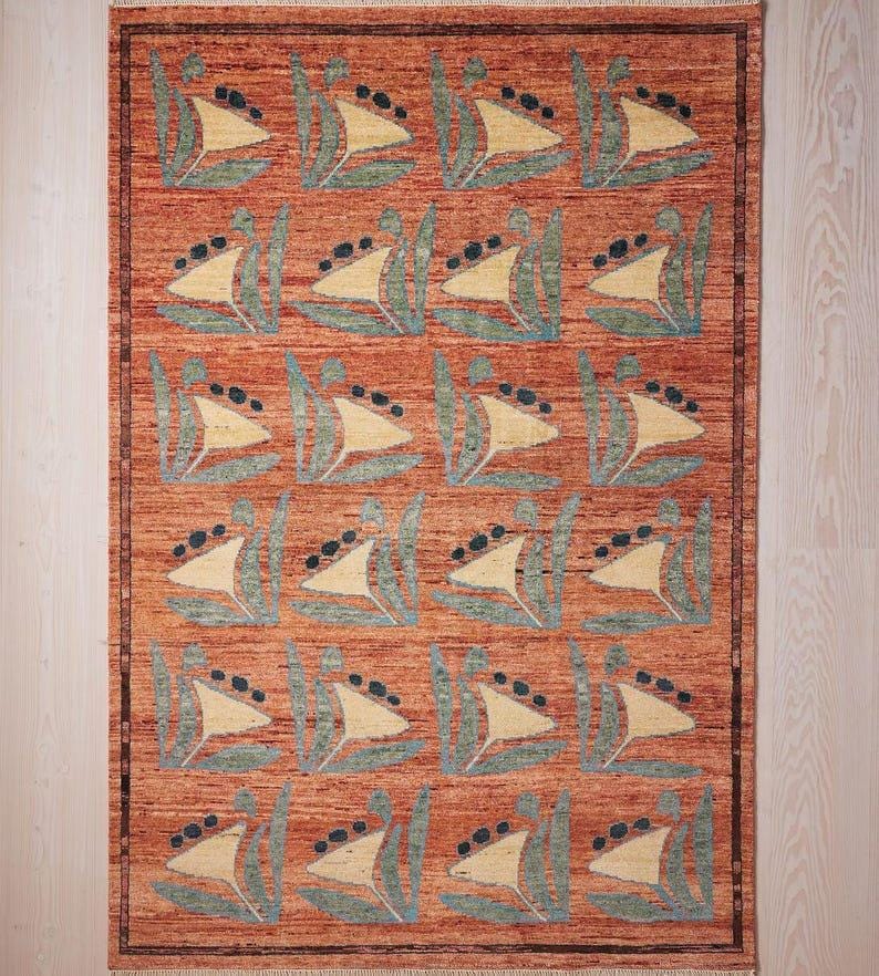 May include: A rectangular rug with a repeating pattern of stylized sailboat motifs. The rug features a warm, reddish-orange background with cream-colored sails, teal accents, and black dots. The rug has a border.
