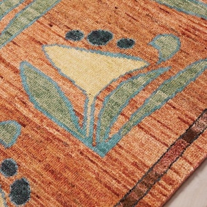 May include: Close-up of a patterned rug with a floral design. The rug features a warm color palette of orange, yellow, and green. The floral pattern is outlined in a teal blue color. The rug has a textured appearance.