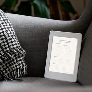 Könnte beinhalten: Ein digitales Tablet mit dem Text "Mein Abend Reset" liegt auf einem grauen Sessel. Eine schwarz-weiß karierte Decke mit Fransen ist über die Armlehne drapiert. Das Tablet zeigt ein Formular mit mehreren Abschnitten.