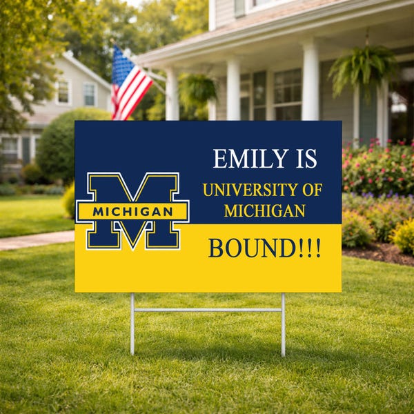 May include: A yard sign with a navy blue and yellow design. The sign features the University of Michigan logo and the text "EMILY IS UNIVERSITY OF MICHIGAN BOUND!!!" displayed on a green lawn with a house and American flag in the background.