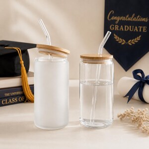 K&ouml;nnte beinhalten: Zwei Glasbecher mit Bambusdeckeln und durchsichtigen Strohhalmen. Einer der Becher ist mattiert, der andere ist klar und mit Wasser gef&uuml;llt. Im Hintergrund befindet sich ein Abschlussbanner mit dem Text "Congratulations GRADUATE".