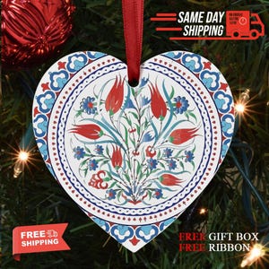 May include: Heart-shaped Christmas ornament with a floral design featuring red tulips and blue flowers on a white background. The ornament has a red ribbon for hanging. The ornament is decorated with a floral pattern.