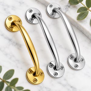 May include: Three curved metal cabinet handles with a polished finish. One handle is gold-toned, and two handles are silver-toned. Each handle features two circular mounting plates, each secured by three visible Phillips head screws at the ends.