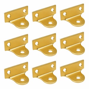 May include: Nine gold-coloured metal picture frame hangers. Each hanger has a rectangular top with two holes and a curved bottom with a single hole. The hangers are arranged in a grid pattern.